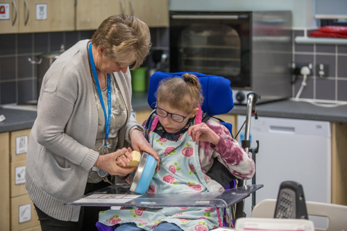 Leaner in a wheelchair grates cheese with teacher