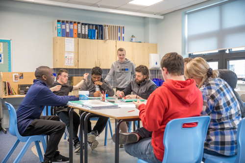 Group of young learners around a classroom table with two teachers