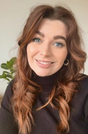 Portrait of Jamie Diwell, a caucasian woman with auburn, curly hair and blue eyes smiling at the camera.