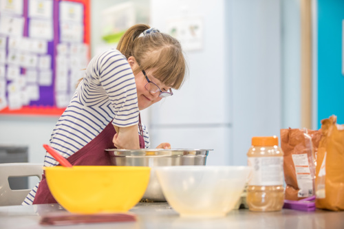 Learner with Downs Syndrome in a stripy top mixes cake batter in a bowl