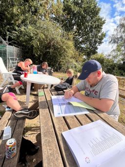 Group of learners writing in ASDAN books on benches outside in the sun