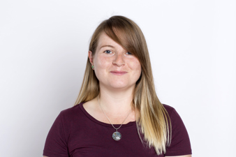 Image of caucasian woman with long dark blonde hair, a pendant necklace an wearing a maroon top.